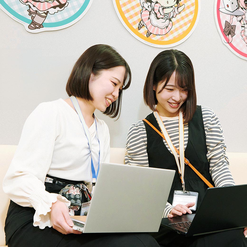 写真：ソファに座って、それぞれノートPCを膝に乗せて画面を見ながら話をしている2人の女性社員